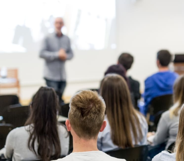 Professor standing up giving a lecture while students sit and listen