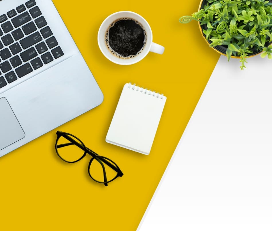 A desk showing a laptop, glasses, and coffee cup